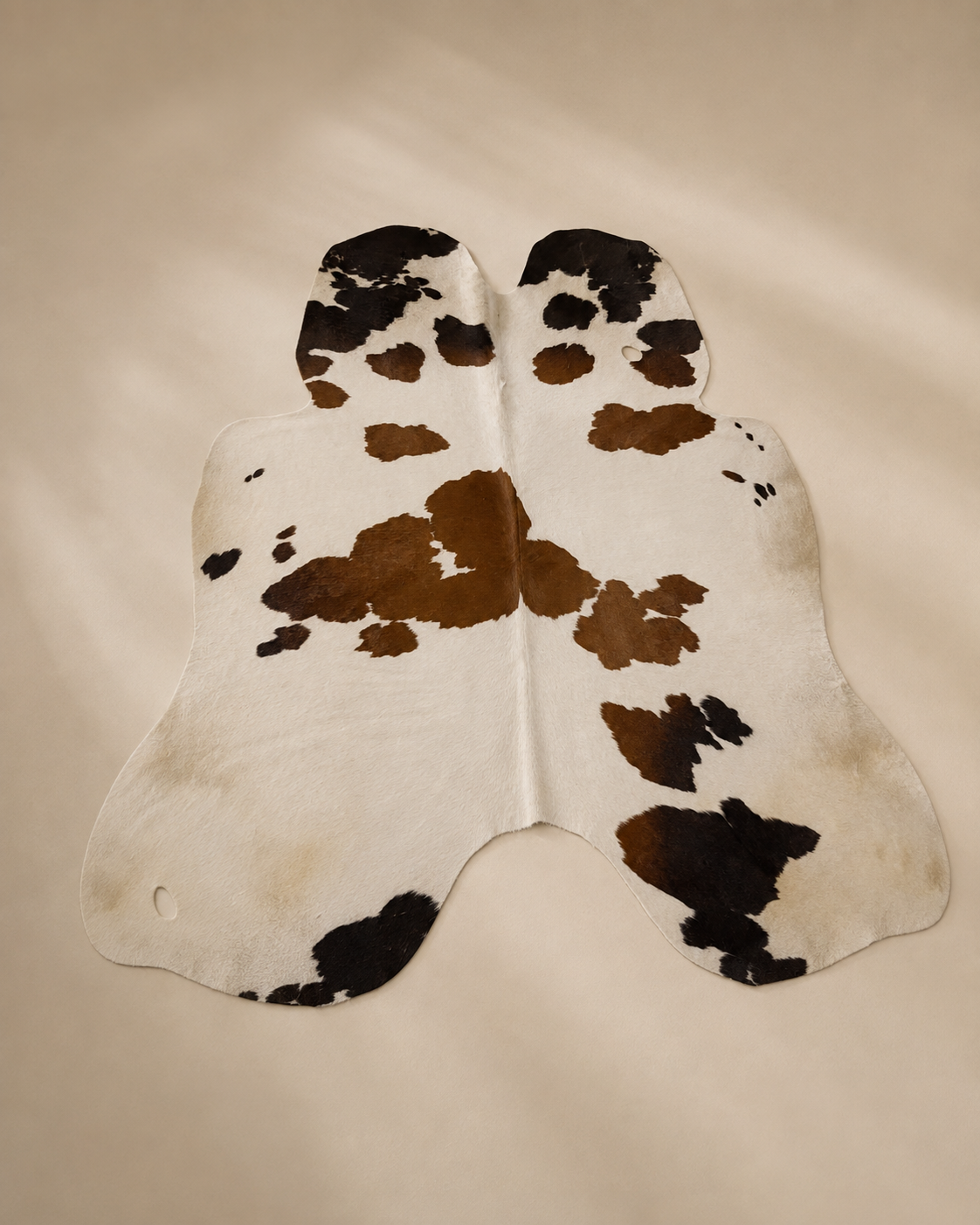 White cowhide rug with brown and black patches on a neutral background